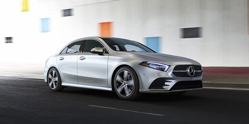 Silver Mercedes-Benz sedan driving on a paved road, captured from the front-left angle