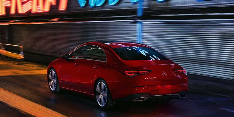 Rear view of a red Mercedes-Benz CLA 250 driving fast on a blurred street at night with neon lights above