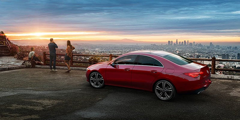 A family views a cityscape with a hazy sunset from a high vantage point, next to a red car