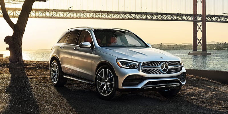 Silver Mercedes-Benz GLC SUV parked beside a waterfront road with a large bridge spanning the background