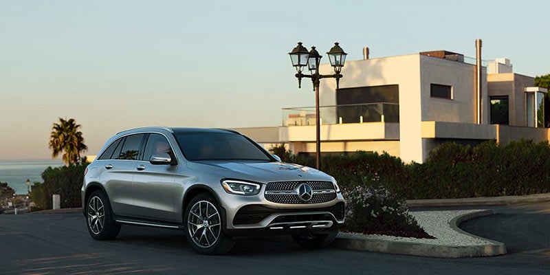 Silver Mercedes-Benz SUV driving through a modern residential neighborhood with contemporary homes and street lamps