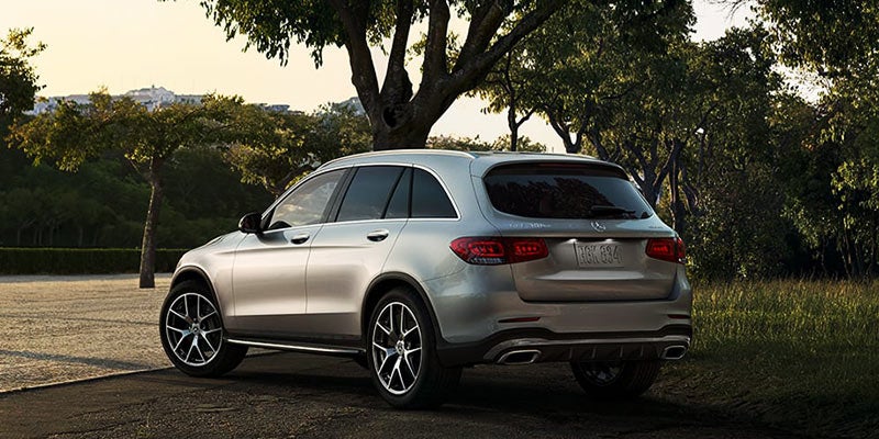 Rear three-quarter view of a silver Mercedes-Benz GLC SUV parked on a tree-lined road in a landscaped outdoor setting