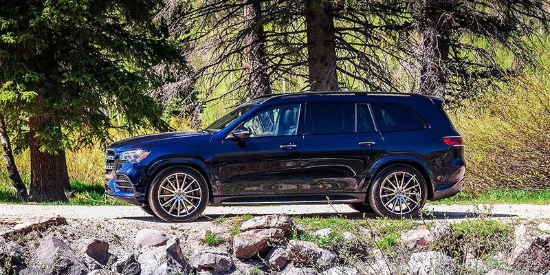 Black luxury SUV parked beside a rocky roadside surrounded by tall trees in a forest setting