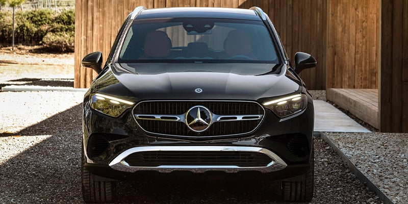 Front view of a black Mercedes-Benz SUV parked on a gravel driveway between wooden-clad buildings