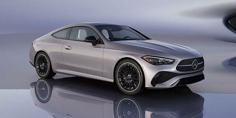 A silver Mercedes Benz CLA coupe with black rims, parked on a reflective surface in a studio