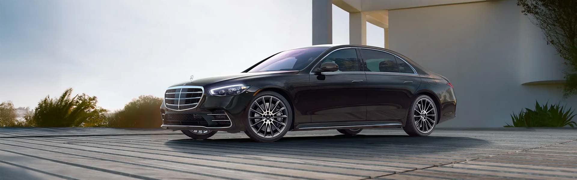 A black Mercedes sedan parked on a wooden deck, with a modern building and foliage in the background.