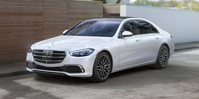 White Mercedes-Benz luxury sedan parked on a paved driveway, viewed from the front-left angle