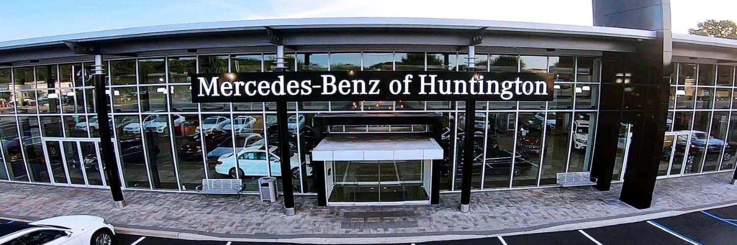 Exterior view of the Mercedes-Benz of Huntington dealership, a modern building with large glass windows and parked cars inside.