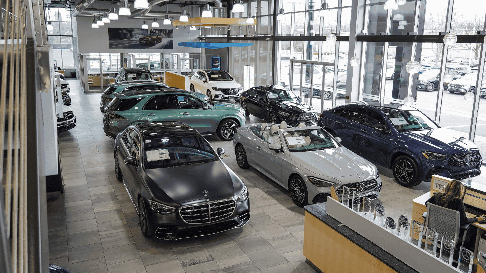 A spacious, well-lit car dealership showroom displaying multiple new Mercedes-Benz sedans, SUVs, and convertibles.
