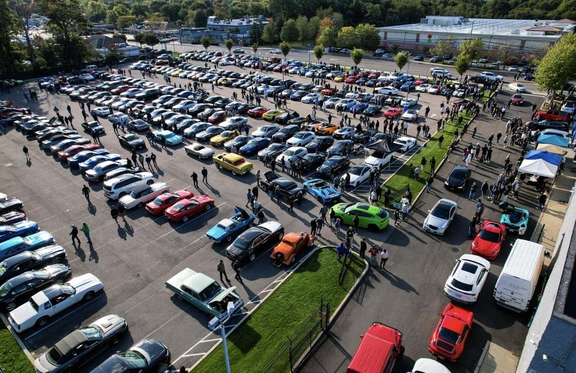 Aerial view of the Cars & Coffee car show with hundreds of vehicles and spectators filling the dealership lot
