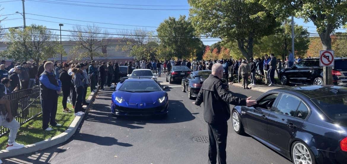 Spectators lining the street as a blue Lamborghini supercar arrives at the show