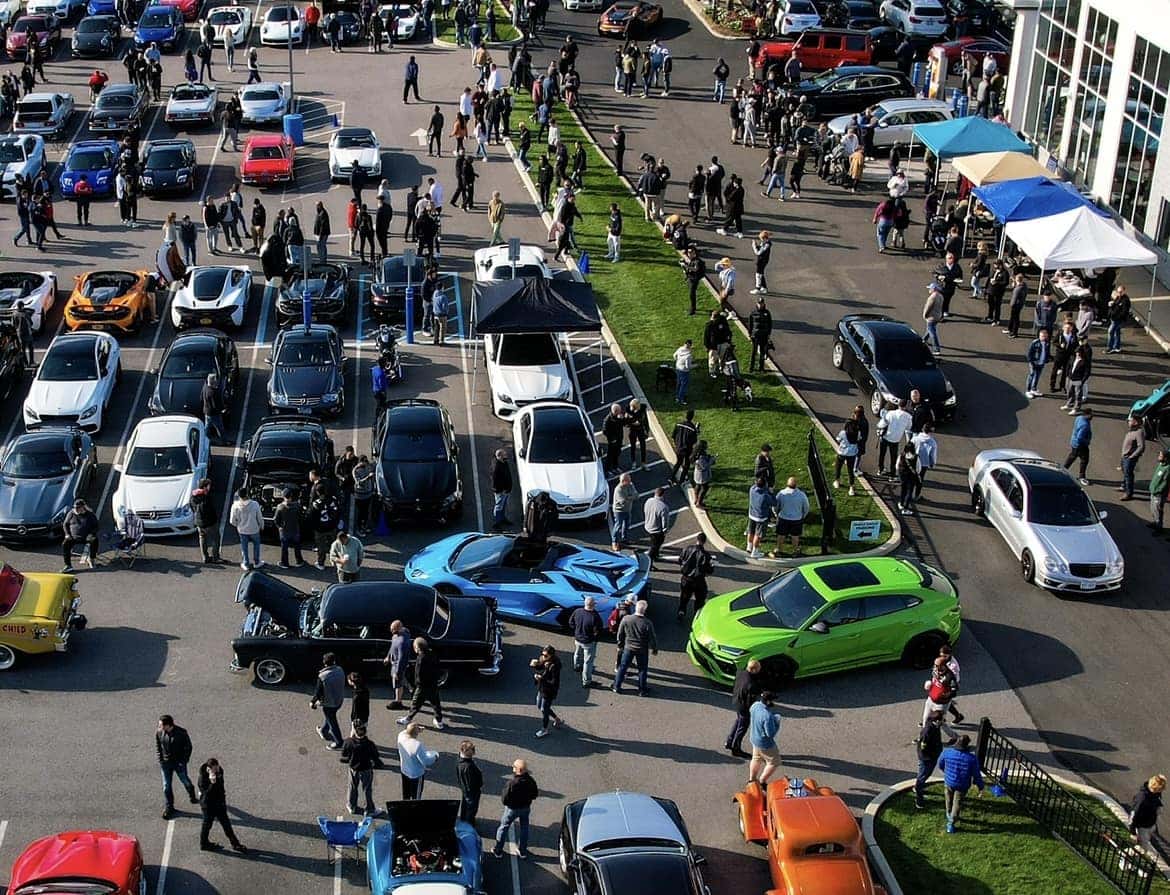 Overhead view of the show rows featuring a green Lamborghini Urus, exotics, and classic cars surrounded by crowds