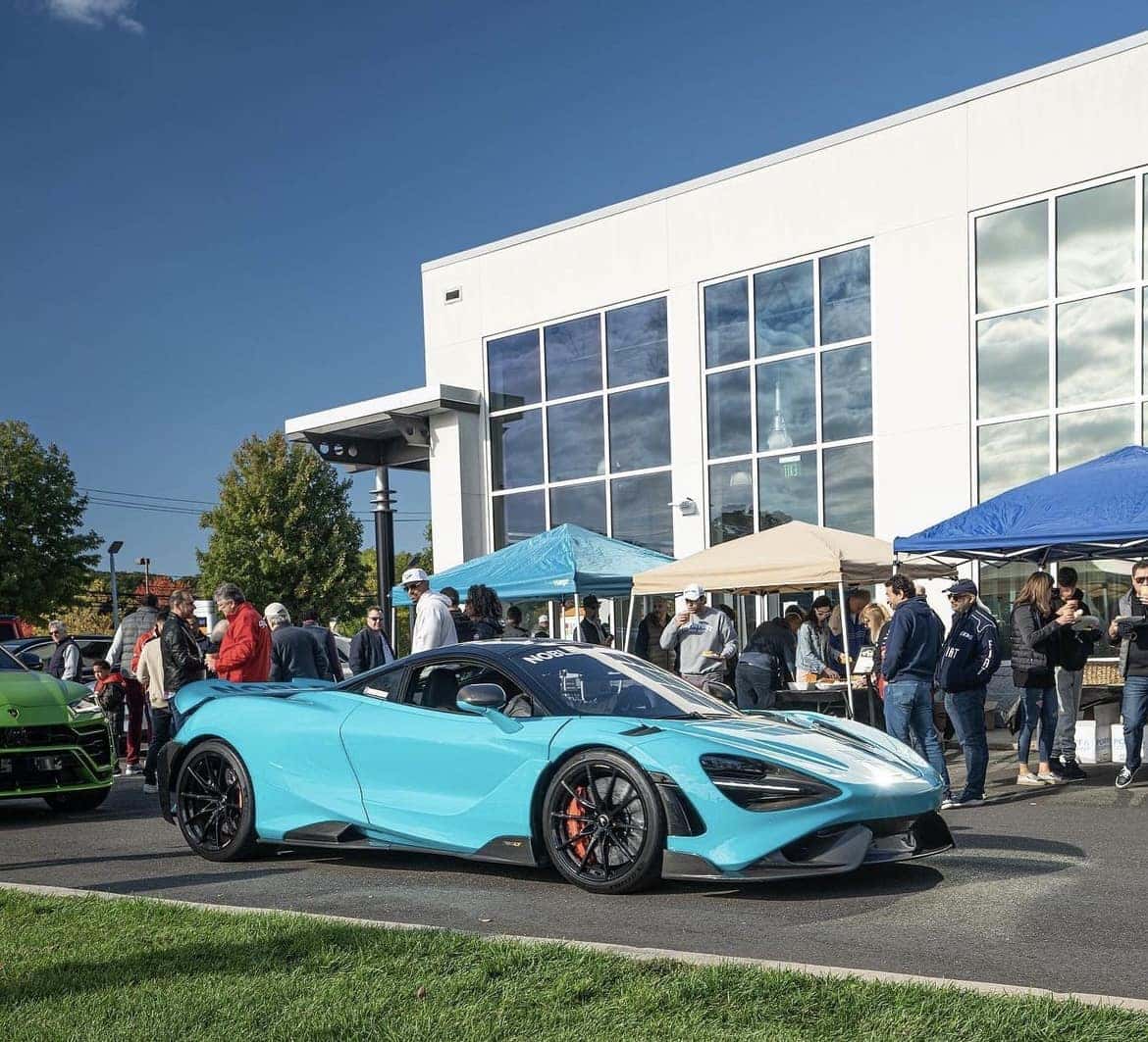 Light blue McLaren 765LT parked in front of the showroom as guests gather under the event tents