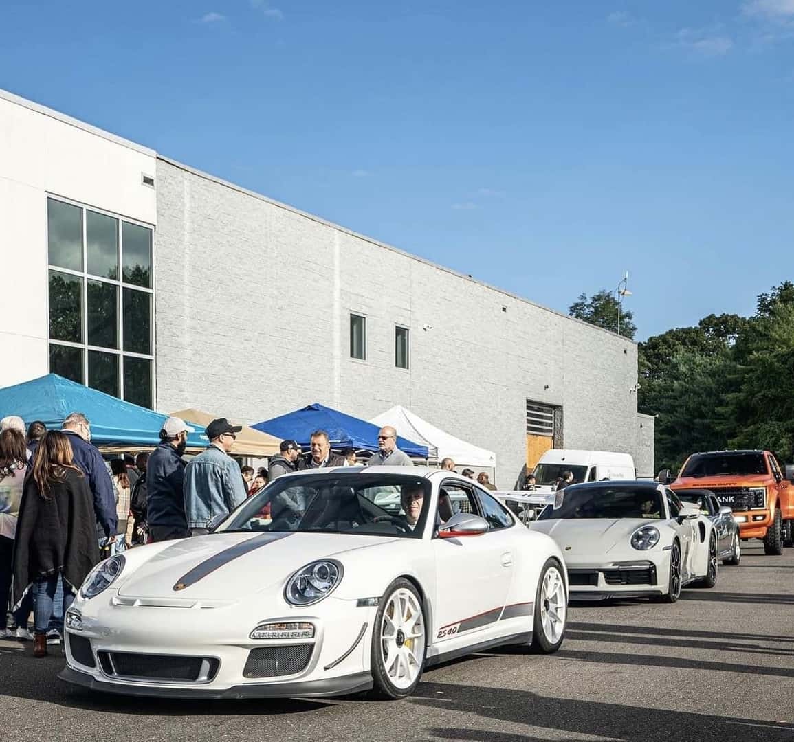 White Porsche 911 GT3 RS leading a line of Porsches past the event tents