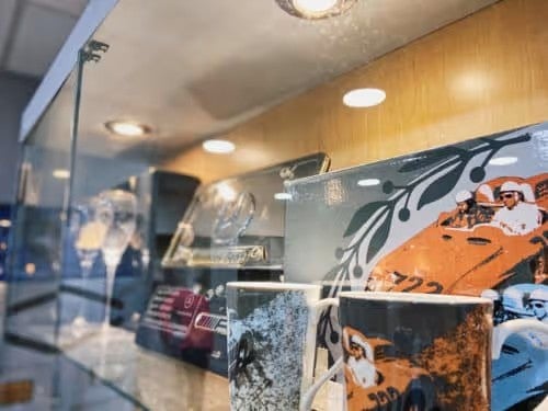 Display case showcasing mugs and trays adorned with illustrations of people in vintage race cars