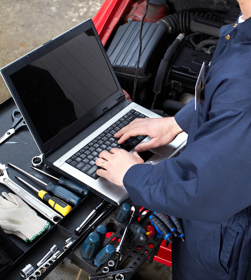 Technician performing vehicle diagnostics on laptop