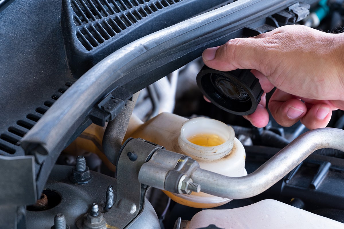 Close-up of a hand removing the cap from a vehicle brake fluid reservoir inside the engine compartment