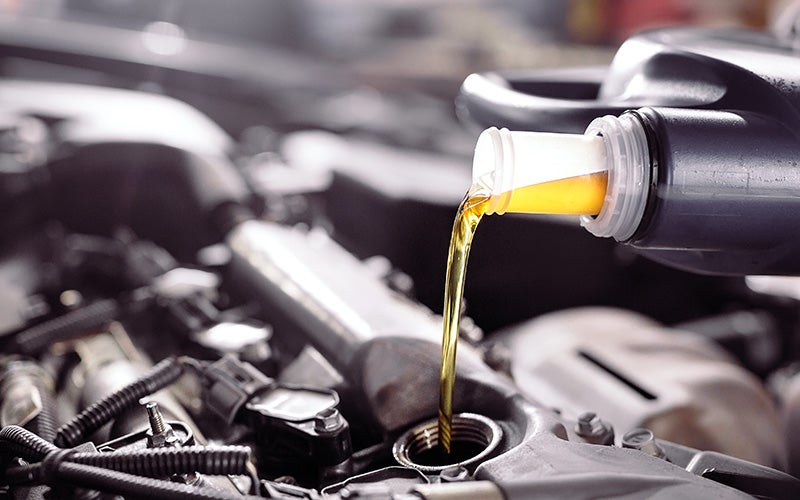 Golden engine oil being poured into a car's engine from a black plastic bottle