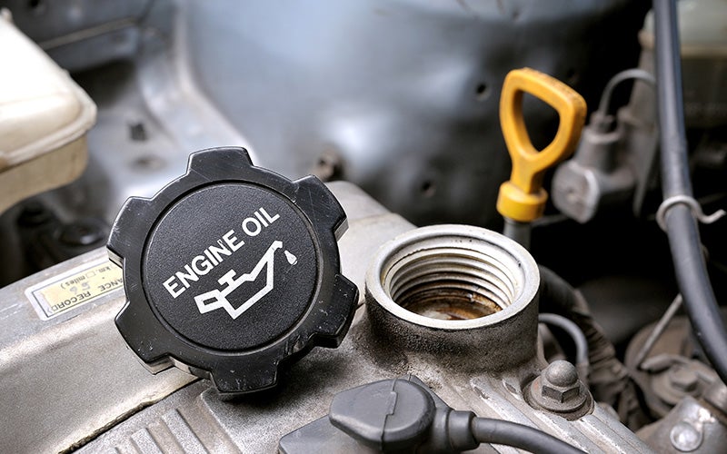 Vehicle engine with the oil filler cap removed, showing the engine oil fill opening and dipstick