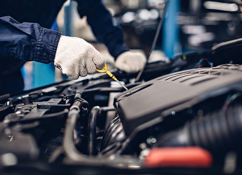 A gloved hand checks the oil with a yellow dipstick in a car engine compartment