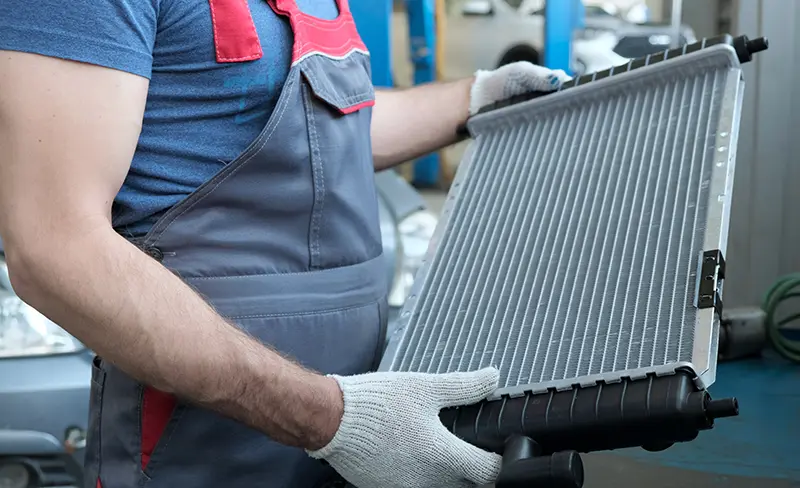 Close-up of an automotive technician holding a vehicle radiator during cooling system maintenance in a repair workshop