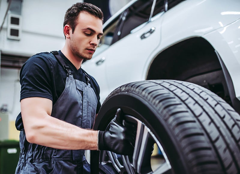 Automotive technician installing a vehicle tire and wheel assembly in a service workshop