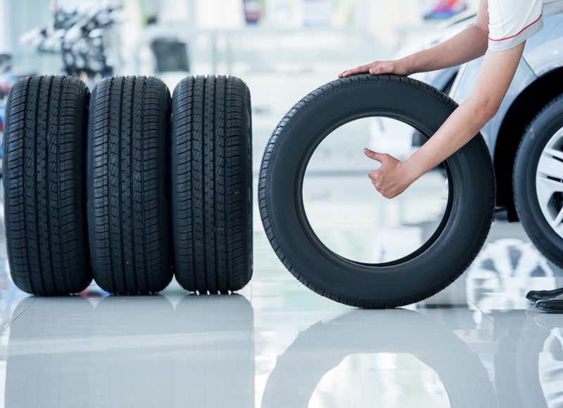Person handling a car tire beside a row of replacement tires in an automotive service center